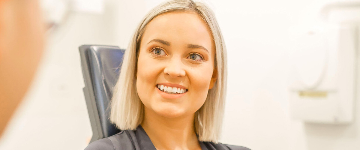 Woman holding dental aligner smiles in conversation with dentist