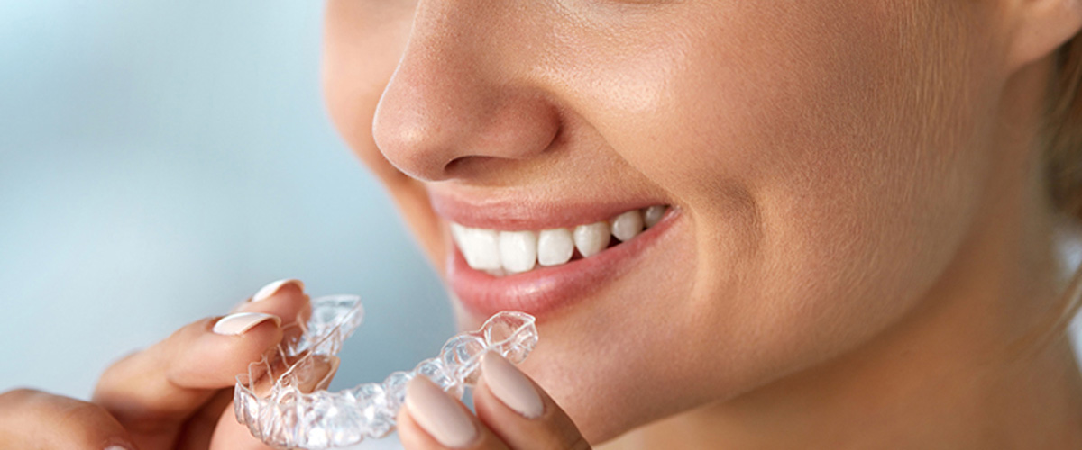 A woman smiling and holding a clear Invisalign tray in front of her mouth